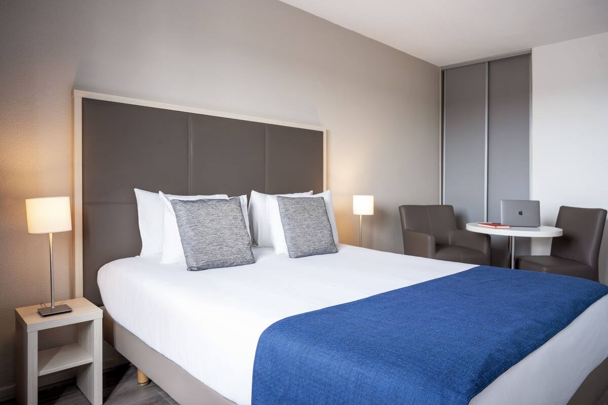 A modern hotel room with a large bed, bedside tables, a desk with a laptop, and a chair.