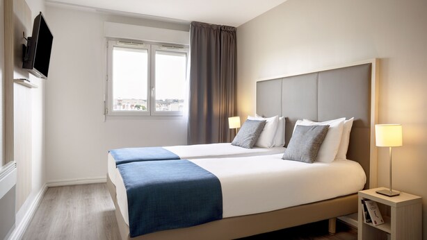 Habitación de hotel con una cama grande, dos mesitas de noche, un televisor montado en la pared y una ventana con cortinas.