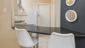 A modern kitchen with a black countertop, white chairs, and a stainless steel range hood.