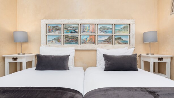 A double bed with white and gray bedding, two bedside tables with lamps, and a wall-mounted picture gallery.