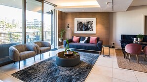 A modern living room with a sofa, armchairs, a coffee table, and a large window offering a city view.