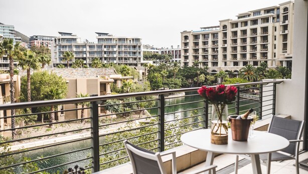 A balcony with a table, chairs, and a view of a river and buildings.