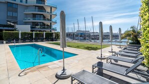 A swimming pool with lounge chairs and umbrellas, surrounded by a modern building with balconies.