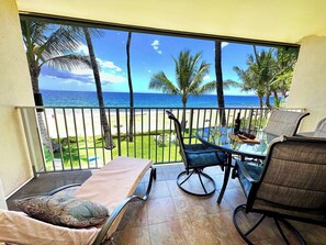 Un balcon avec vue sur la plage, une table avec des chaises et un fauteuil de relaxation.