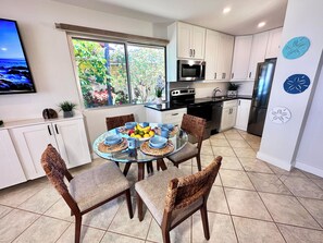A modern kitchen with white cabinets, a stainless steel refrigerator, and a dining area with a glass table and wicker chairs.