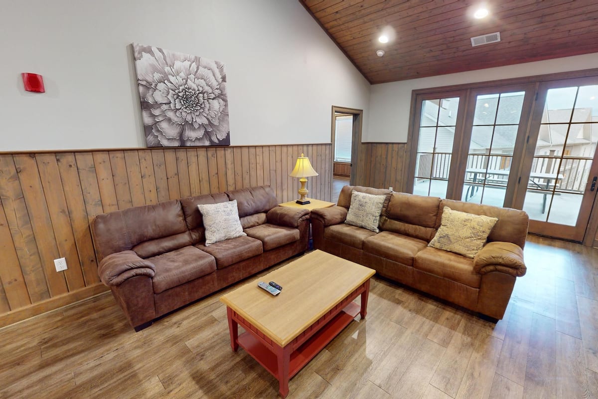 A spacious living room with two brown leather sofas, a wooden coffee table, and a large window providing a view of the outside.
