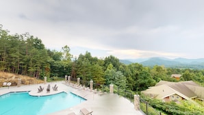 A swimming pool with lounge chairs and a view of a forest and mountains.