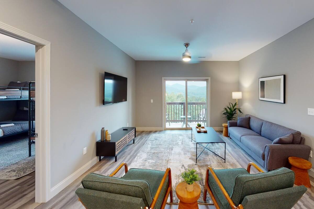 A modern living room with a sofa, chairs, a TV, and a balcony with a view.