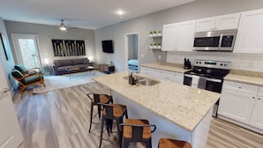 A modern kitchen with white cabinets, a granite countertop, and stainless steel appliances. There is a dining area with a wooden table and chairs.