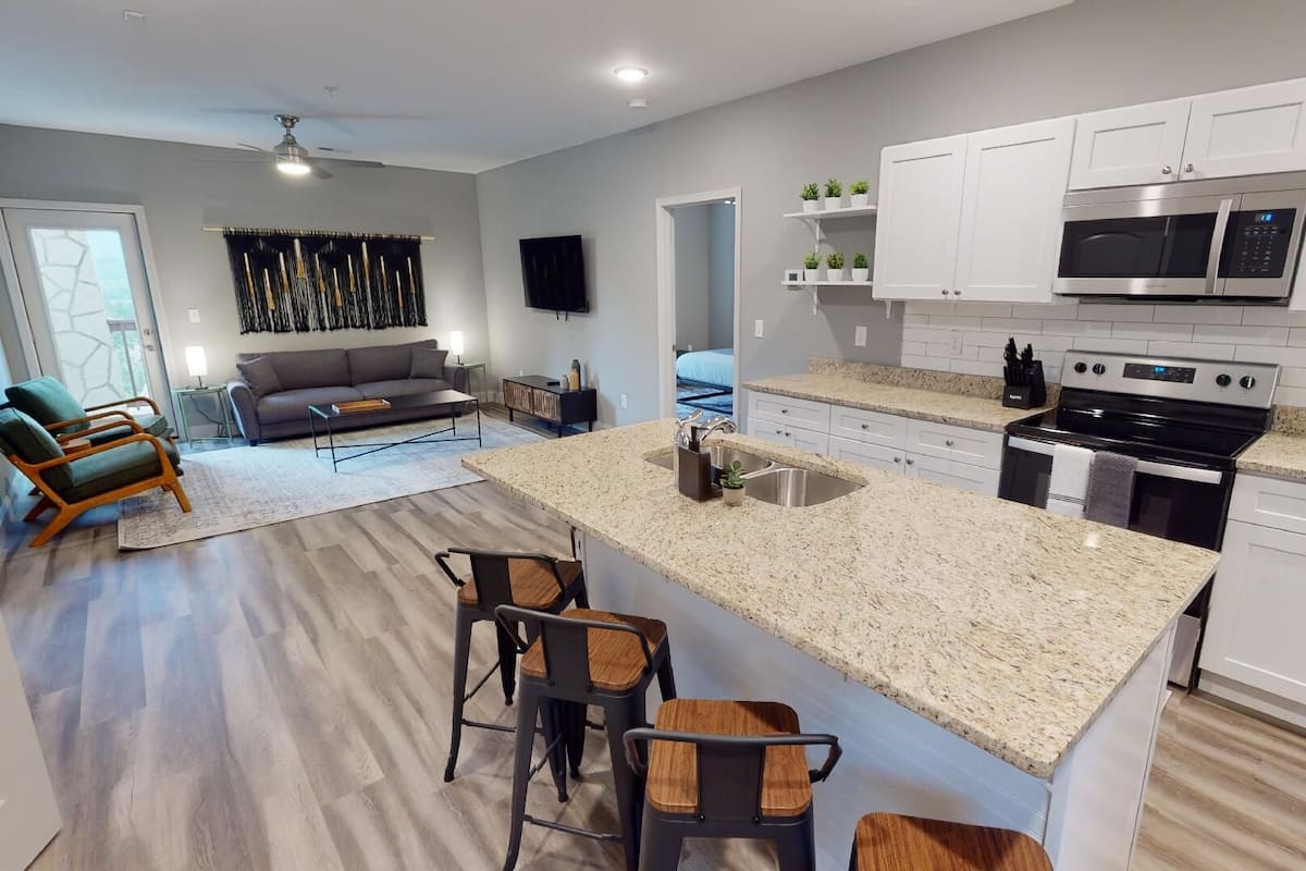 A modern kitchen with white cabinets, a granite countertop, and stainless steel appliances. There is a dining area with a wooden table and chairs.