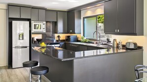 A modern kitchen with grey cabinets, a stainless steel refrigerator, a microwave, and a large island with stools.