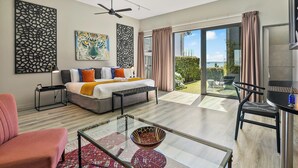 A modern hotel room with a bed, a glass coffee table, a sofa, a chair, and a view of the outdoors.