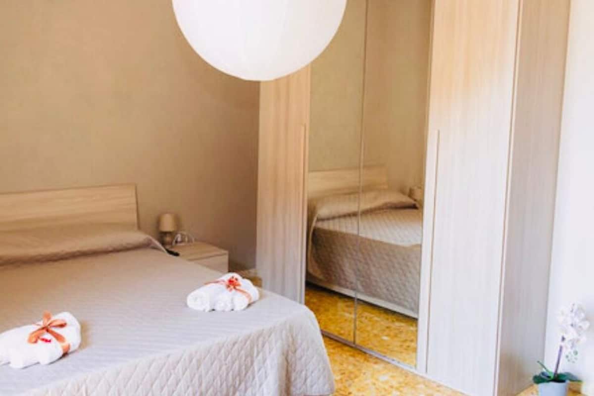 Une chambre d’hôtel avec un lit, une table de chevet, un miroir et une plante en pot.
