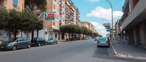 Vista da rua com edifícios altos, carros estacionados e céu claro.