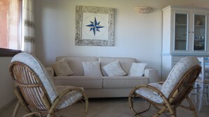 A living room with a beige sofa, two wicker chairs, a wall-mounted compass decoration, and a cabinet with glass doors.
