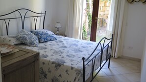 A bedroom with a bed, a bedside table, a lamp, and a view of the outside.