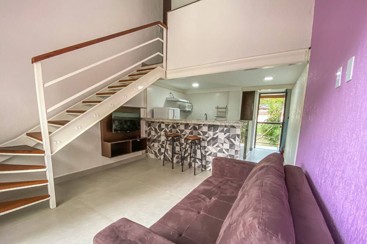 Un intérieur moderne avec un escalier, un espace de vie doté d’un canapé violet et une cuisine agrémentée d’un pare-feu géométrique.