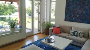 Amplia sala de estar con un gran ventanal, un sofá color beige, una mesa de centro blanca y una alfombra azul.