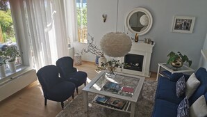 Un salón con un sofá azul, una mesa de centro y una chimenea. Hay plantas en macetas y un espejo en la pared.