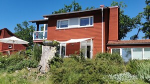 Una casa roja de dos pisos con balcón, rodeada de follaje y un paraguas blanco.