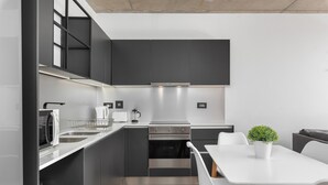 Una cucina moderna con mobili scuri, un piano di lavoro bianco e un'area pranzo con tavolo e sedie bianche.