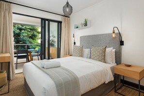 Habitación de hotel moderna con una cama grande, una mesita de noche, un escritorio y un balcón con vistas a zonas verdes.