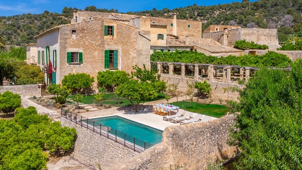 Un edificio de piedra con piscina, rodeado de vegetación y colinas.