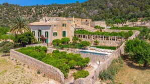 Una villa con piscina, rodeada de exuberante vegetación y muros de piedra.