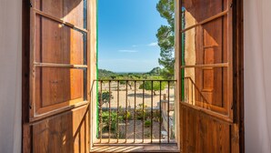 Un balcón de madera con vista a un jardín ajardinado y colinas al lejano.
