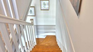 A staircase with white railings and wooden steps leading to a landing with framed artwork and a painting on the wall. - Avaugour Vacation Rental: 5 bedrooms, 1 accessible for people with disabilities, in the Côtes d'Armor region of Brittany (Saint-Fiacre)