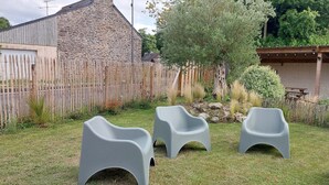 A backyard with a stone building, a wooden fence, and three gray plastic chairs. - Avaugour Vacation Rental: 5 bedrooms, 1 accessible for people with disabilities, in the Côtes d'Armor region of Brittany (Saint-Fiacre)