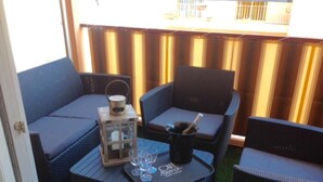Un espacio exterior con mobiliario de mimbre y una mesita con vasos y una botella.