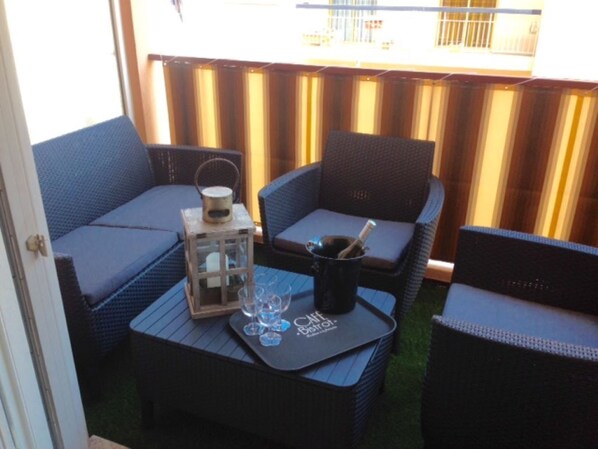 An outdoor seating area with wicker furniture and a tray table with glasses and a bottle.
