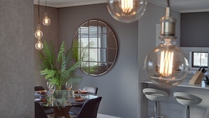 A modern dining area with a round mirror, potted plants, and hanging light fixtures. - Intaka Facing 2-Bedroom Gem (Cape Town)