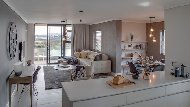A modern living room with a sofa, dining area, and kitchen. - Intaka Facing 2-Bedroom Gem (Cape Town)