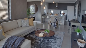 A modern living room with a sofa, coffee table, and a dining area with chairs and a table. - Intaka Facing 2-Bedroom Gem (Cape Town)