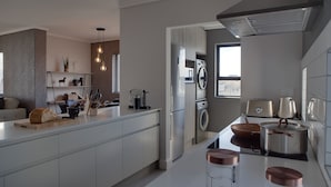 A modern kitchen with a central island, built-in appliances, and a view to the outside. - Intaka Facing 2-Bedroom Gem (Cape Town)