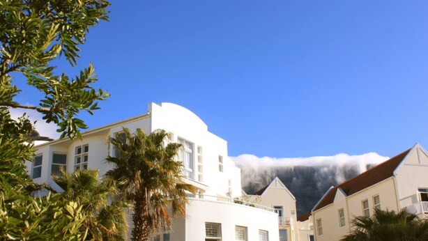 A white building with a curved roof and multiple windows, surrounded by palm trees and other buildings. - Exclusive Townhouse with Stunning Views (Cape Town)