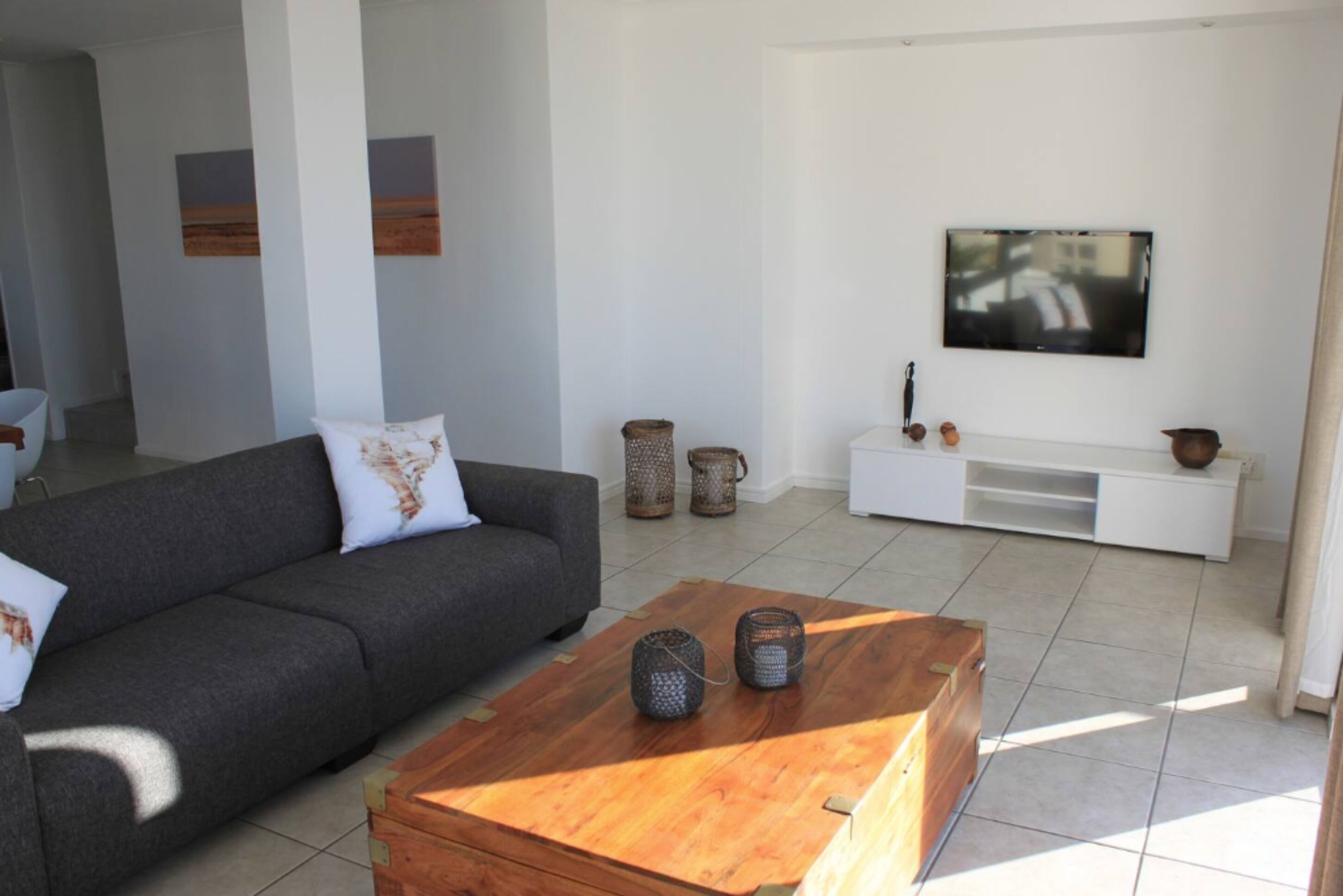 A modern living room with a grey sofa, wooden coffee table, and a flat-screen TV mounted on the wall.