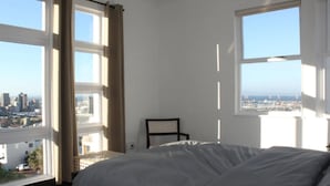 A bedroom with a bed, a chair, and large windows offering a city view. - Exclusive Townhouse with Stunning Views (Cape Town)