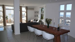 A spacious living area with a wooden dining table, white chairs, a dark sofa, and a balcony with a view. - Exclusive Townhouse with Stunning Views (Cape Town)