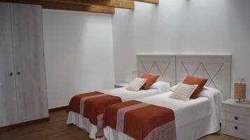 A bedroom with two beds, wooden flooring, white walls, and a wooden ceiling beam.