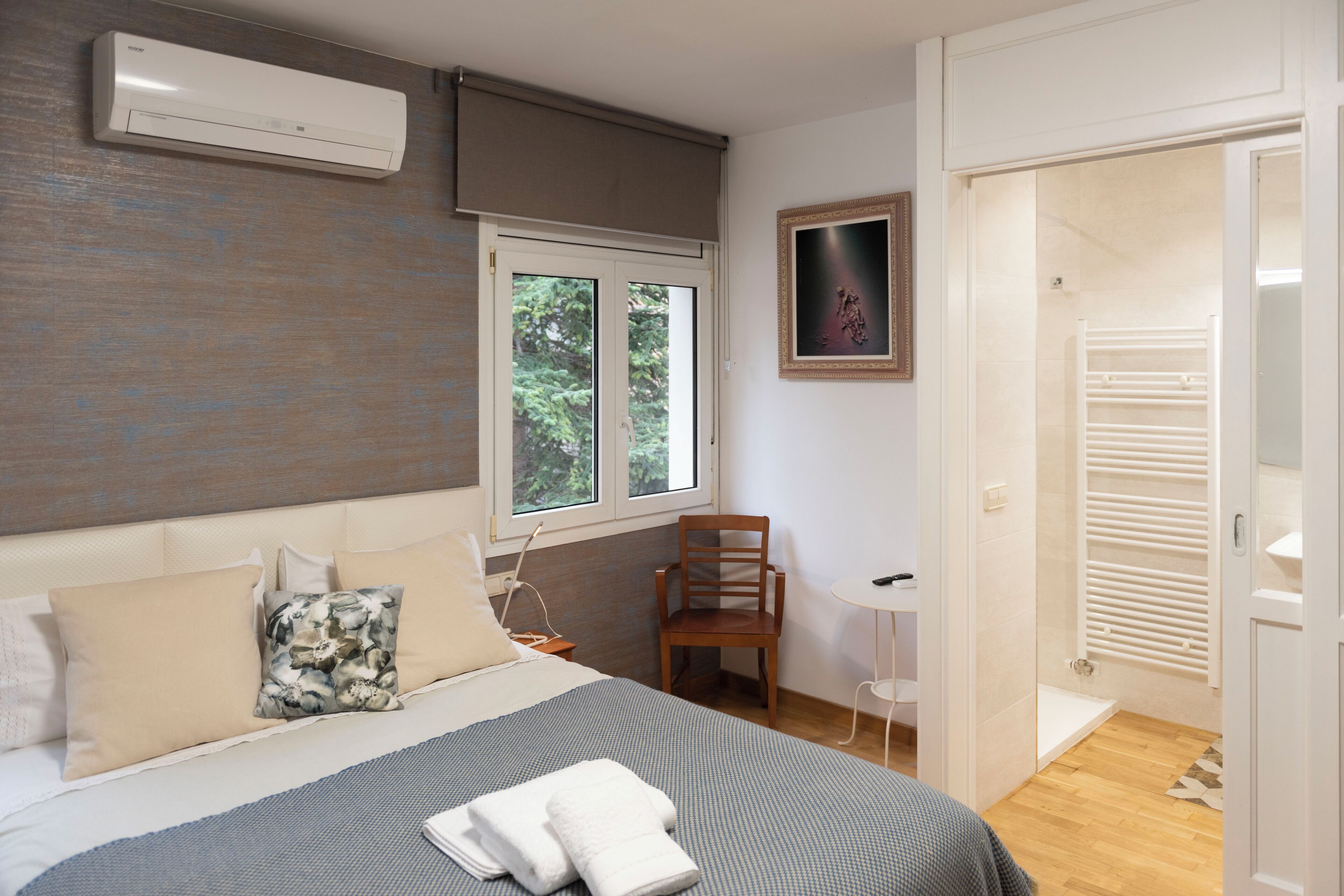 A bedroom with a bed, a chair, a small table, and a window with a view of trees.