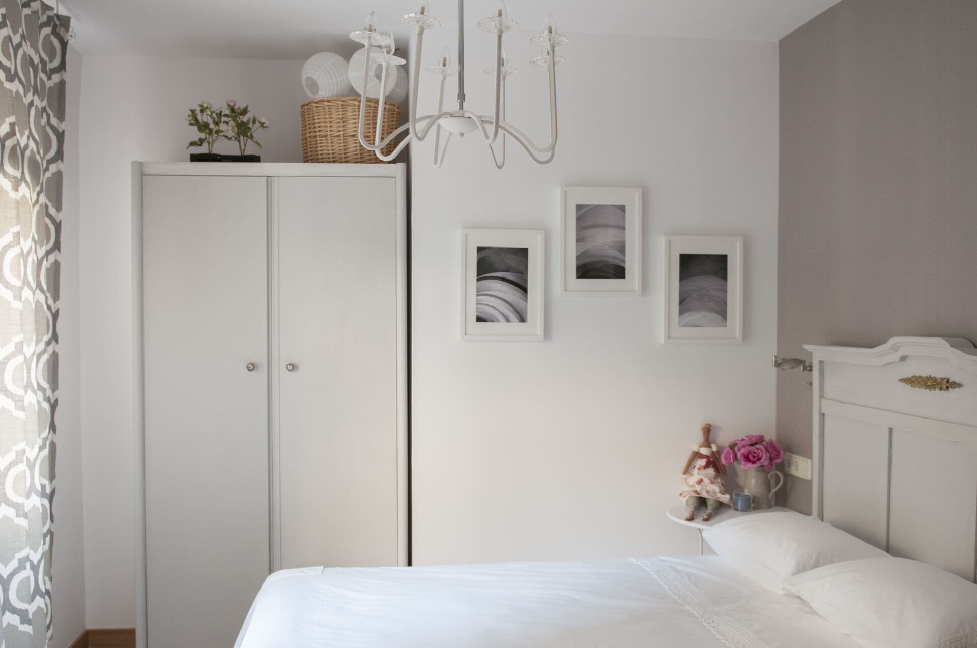 Een slaapkamer met een bed, een kledingkast, een kroonluchter en foto's aan de muur.
