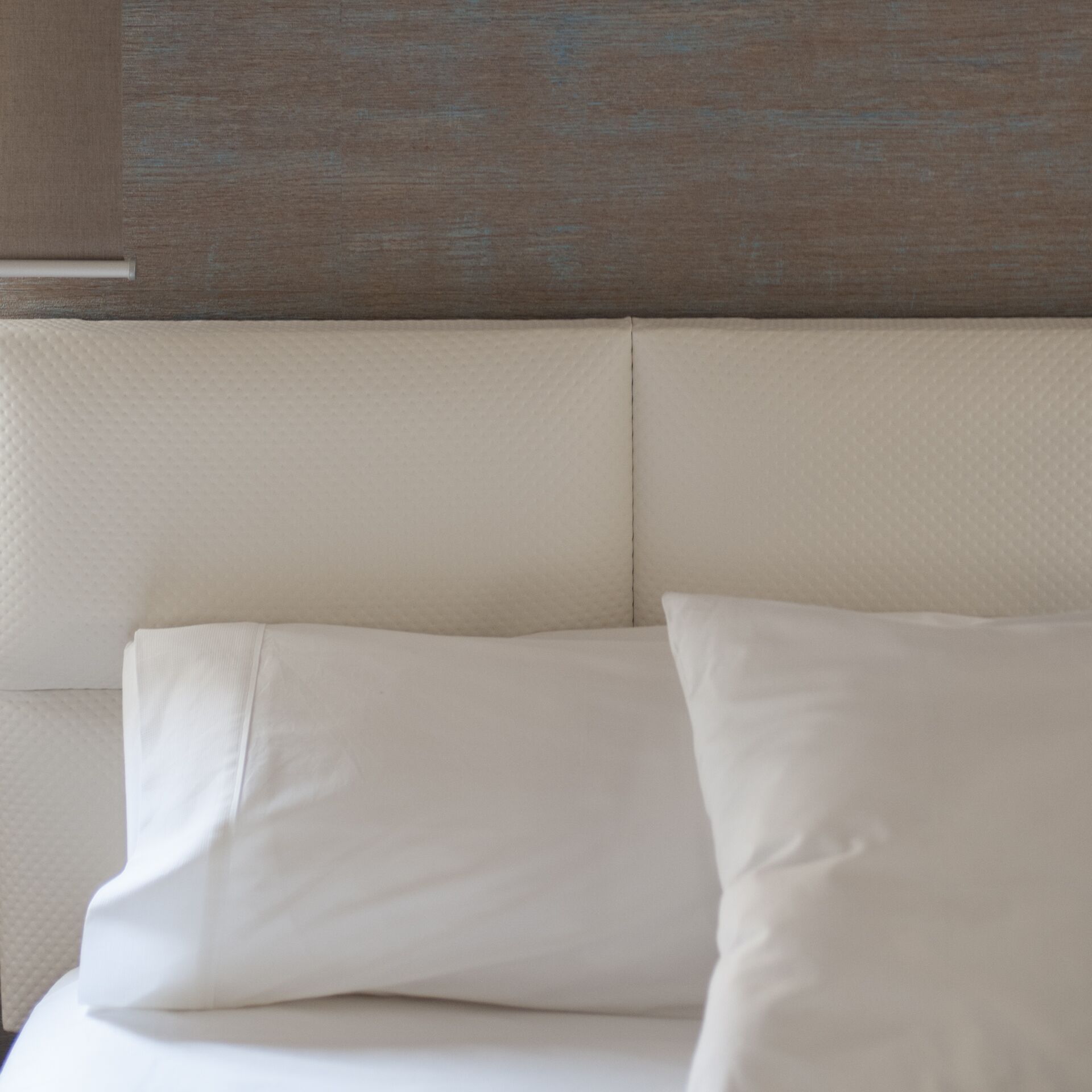 Parte de una habitación con una pared texturizada y un cabecero tapizado en blanco.