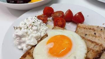 A breakfast plate with a fried egg, tomatoes, and a bowl of fruit.