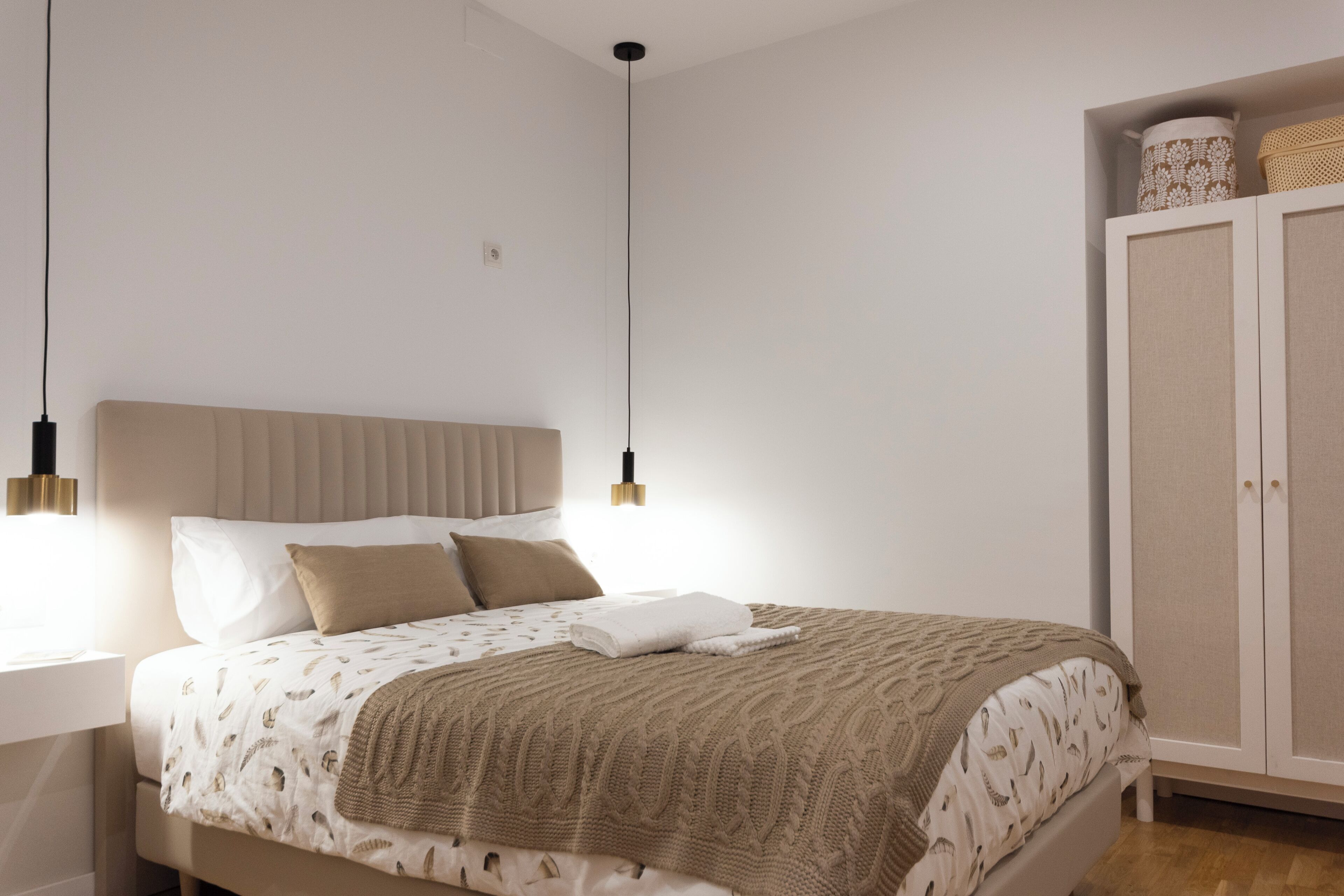 A bedroom with a bed, bedside table, wardrobe, and pendant lights.