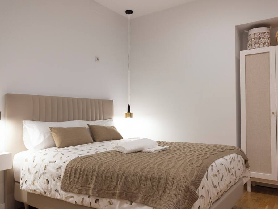 Un dormitorio con cama, mesita de noche, armario y lámparas colgantes.