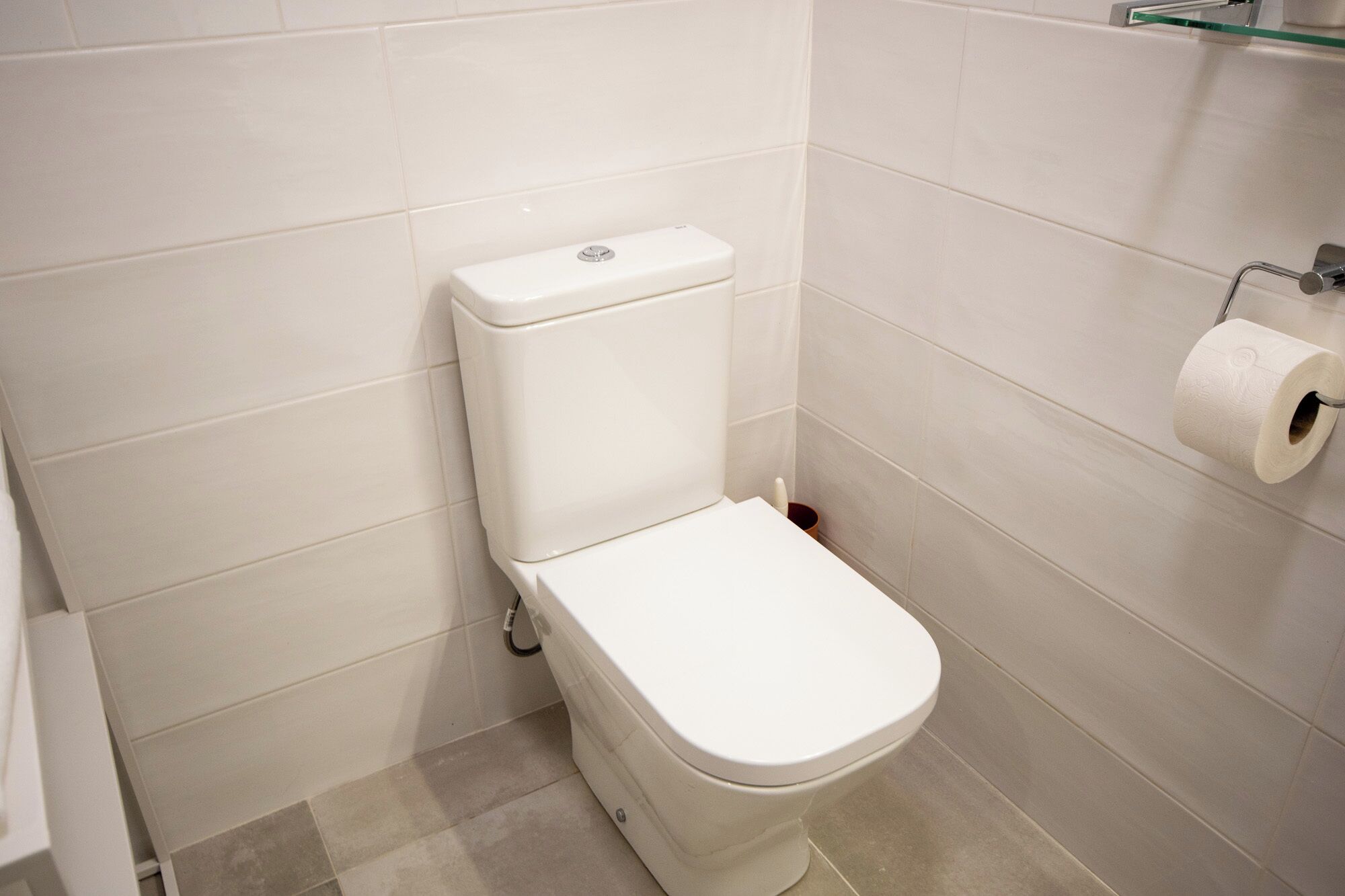 Un inodoro blanco en un baño con azulejos blancos en las paredes y el suelo.