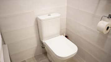 Un inodoro blanco en un baño con azulejos blancos en las paredes y el suelo.